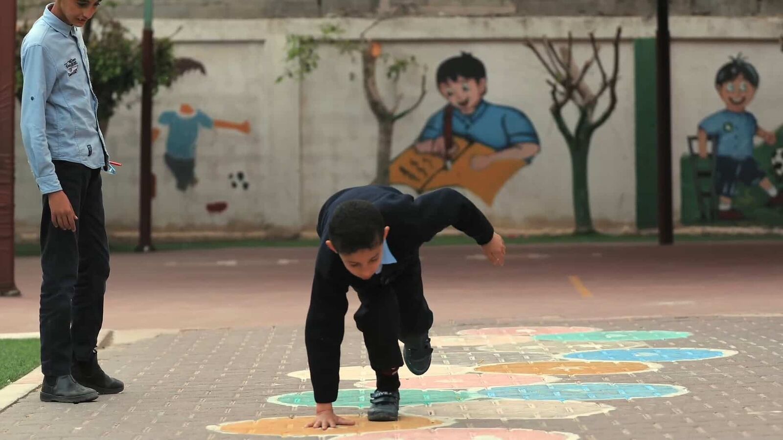 Children play in a schoolyard in Gaza; one balances upside down on the painted ground.